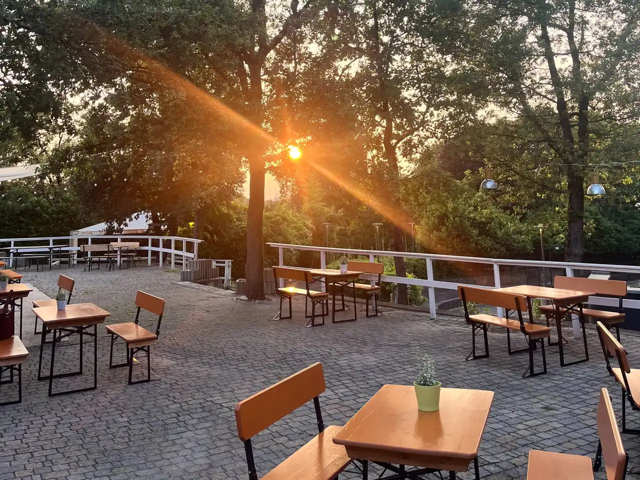 Il tramonto fra gli alberi sopra la terrazza del ristorante, con i tavoli e le panche di legno vuoti.