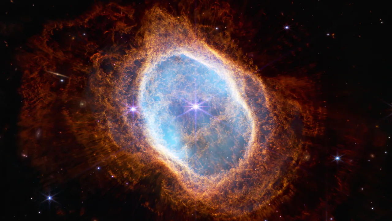 Un guscio ovale di gas azzurro, circondato da strati di filamenti arancioni, al centro di un fondo nero con poche stelle. È la nube lasciata da una stella al termine della sua vita.